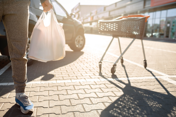 Close-up of a stroller with food near a large supermarket in a suburban shopping center. A man stands near a car in a parking lot after a successful shopping - Φωτογραφία, εικόνα