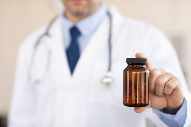 Зрелый опытный врач держит банку для таблеток
 - Фото, изображение