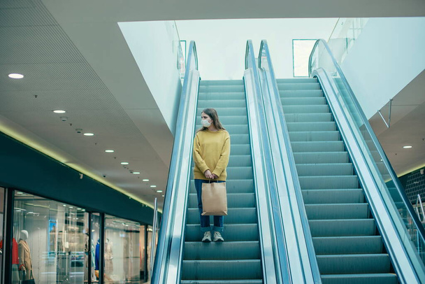 lone woman in a protective mask standing on the escalator steps - Fotoğraf, Görsel