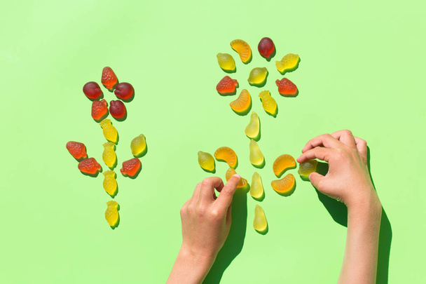 Childs 'ın elleri jöleli meyve şekerlerinden çiçek yapıyor, nane yeşili arkaplanda tatlılar. Çocuk sanatları ve el sanatları, yaratıcı sanat eserleri, diy, kendi kendine eğlence, eğitim, öğrenme konsepti - Fotoğraf, Görsel