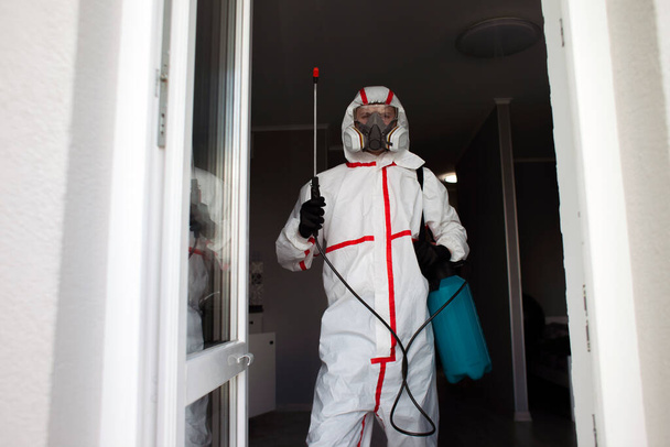 dezynfekcja koronawirusów wewnątrz domu. Dezynfektor w Hazmat oczyszcza mieszkanie z wirusów i infekcji rozpylaczem antybakteryjnym - Zdjęcie, obraz