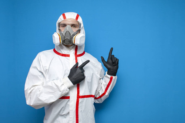 professional disinfector man in a protective suit shows a place for text on a blue isolated background, disinfection service worker, coronavirus concept - Photo, Image