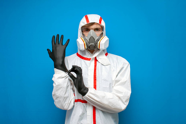 профессиональный дезинфицирующий человек в защитном костюме носит перчатки на синем изолированном фоне, работник службы дезинфекции, коронавирусная концепция
 - Фото, изображение