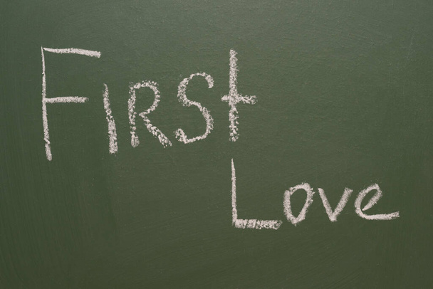 Handwritten inscription in chalk First love on a green board - Фото, изображение