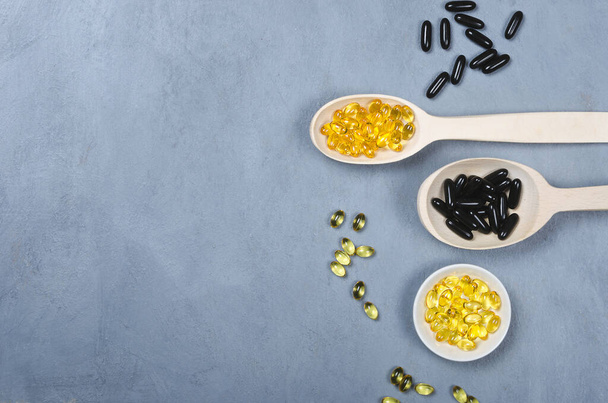 Black pills and yellow pill on wooden spoons on grey background - Photo, Image