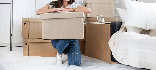 young woman with a cardboard box sitting on the floor in a new apartment - Foto, afbeelding