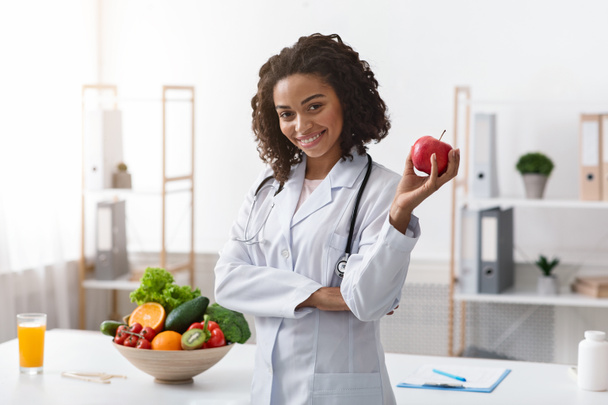 Pozytywna kobieta, pozująca w klinice, trzymająca jabłko - Zdjęcie, obraz