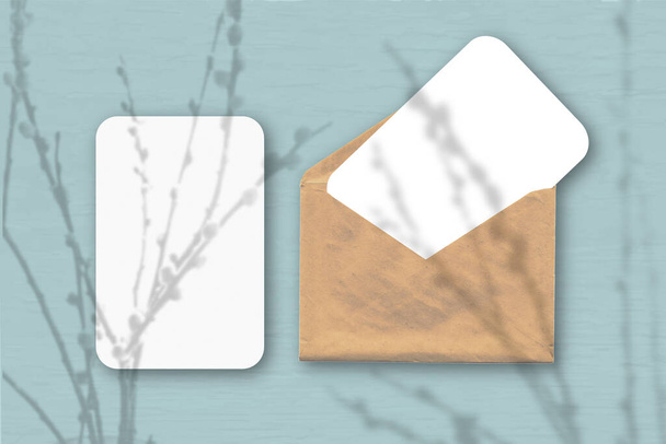 Ένας φάκελος με δύο φύλλα λευκού χαρτιού σε γκρι φόντο τραπεζιού. Mockup με μια επικάλυψη των σκιών των φυτών. Φυσικό φως ρίχνει σκιές από κλαδιά ιτιάς. - Φωτογραφία, εικόνα