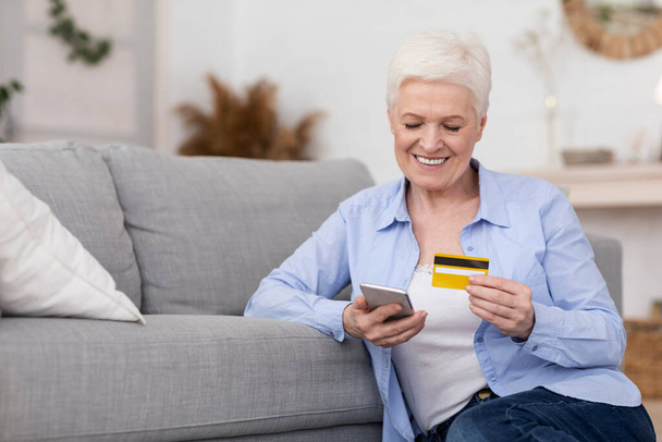 Ηλικιωμένη γυναίκα ψωνίζει online με smartphone και πιστωτική κάρτα στο σπίτι - Φωτογραφία, εικόνα