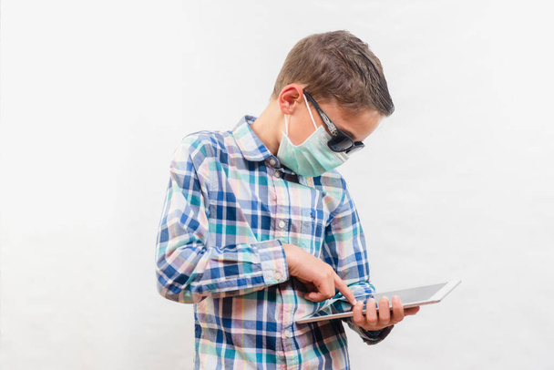 School boy wearing disposable mask and sunglasses holding tablet over white background. Homeschooling concept - Valokuva, kuva