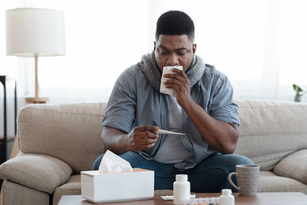 Symptoms Of Coronavirus. Sick african man checking body temperature at home - Fotografie, Obrázek