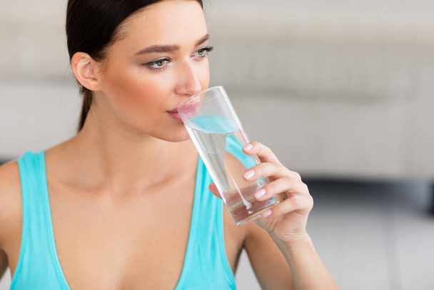 Menina desportiva beber copo de água sentado em casa
 - Foto, Imagem