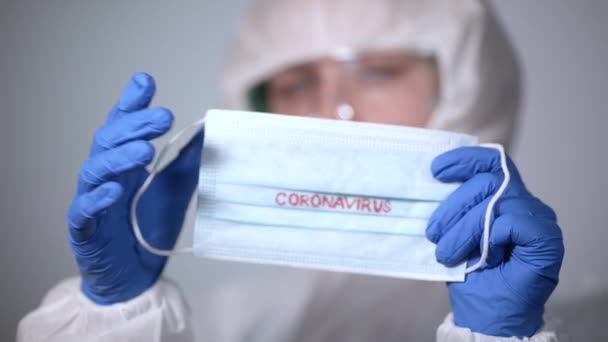 COVID-19. 2019 Novel Coronavirus (2019-nCoV) concept. Young girl doctor in a white protective anti-plague coat holding a medical mask with the inscription Coronavirus - Filmati, video