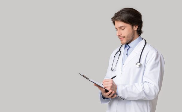 Mladý lékař přezkoumává anamnézu pacientů a zapisuje si poznámky do schránky - Fotografie, Obrázek
