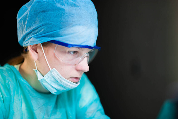 Female doctor in uniform, glasses and mask works concentrated in the hospital. portrait of a surgeon - Фото, зображення