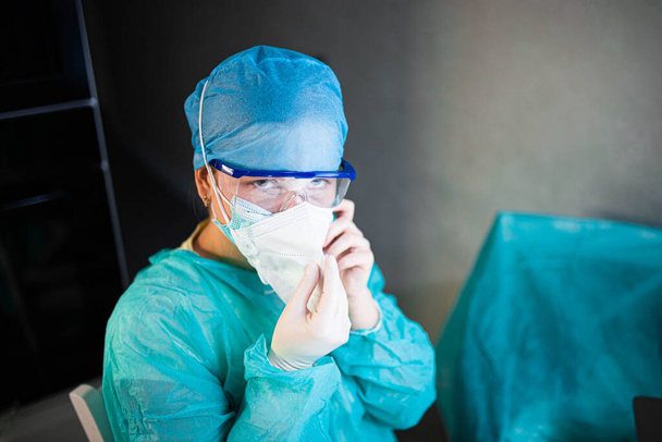 Female doctor in uniform, glasses and mask works concentrated in the hospital. portrait of a surgeon - 写真・画像