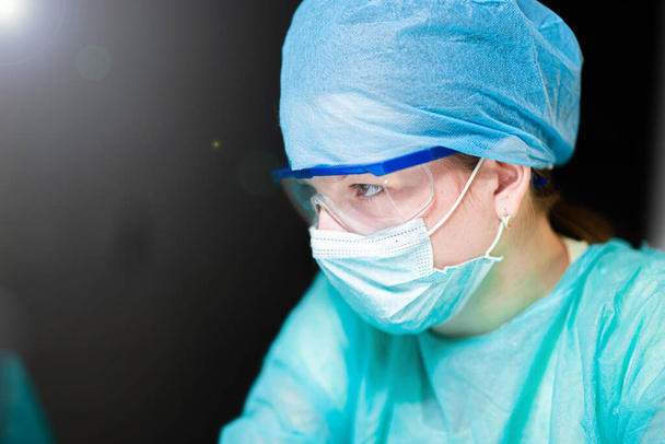 Female doctor in uniform, glasses and mask works concentrated in the hospital. portrait of a surgeon - Foto, immagini