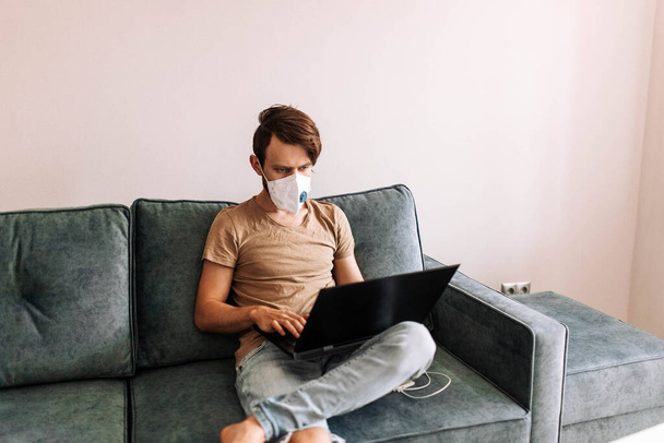 man in a medical mask works with a laptop at home, quarantine self-isolation. - 写真・画像