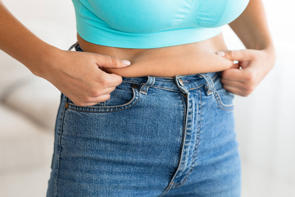 Mujer irreconocible tocando el estómago caído después del aumento de peso en casa
 - Foto, imagen