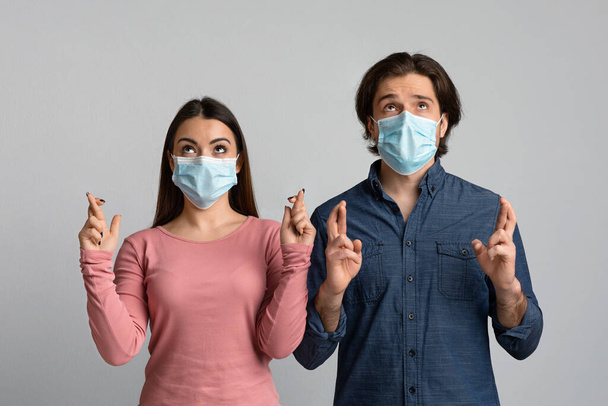 Couple superstitieux en masques médicaux croisant les doigts dans l'espoir de lutter contre le coronavirus
 - Photo, image