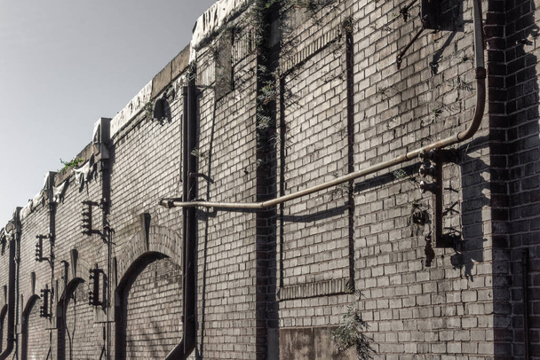 Blick entlang der Fassade eines Industrielagergebäudes, alte Ziegel und Rohre, horizontaler Aspekt - Foto, Bild