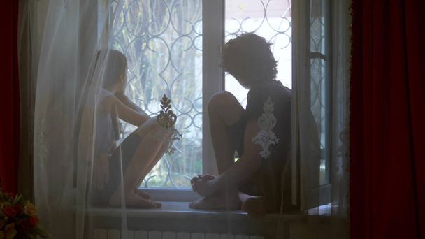 teenage brother and sister are sitting on the windowsill behind the tulle. - Foto, Imagen