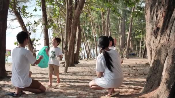 Батько азіатської сім'ї, мати, син і дочка допомагають один одному збирати сміття, пластикові пляшки в зелений пластиковий пакет на пляжі. Безпечна екологія і концепція переробки. Повільний рух - Кадри, відео