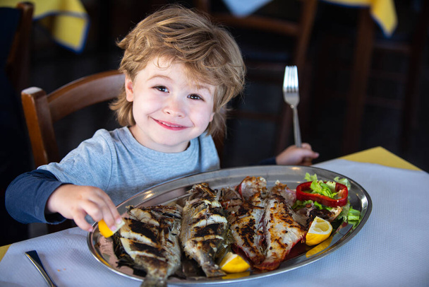 Restaurantessen zu Hause. Kochen während der Quarantäne. Die Tradition der Familienessen zu Hause während der Sperrung. Der Junge isst Fisch am Tisch. Meeresabendessen. - Foto, Bild