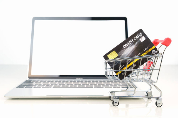 Cartão de crédito no carrinho de compras frente da tela em branco do laptop para compras on-line no branco, trabalho do conceito home
 - Foto, Imagem