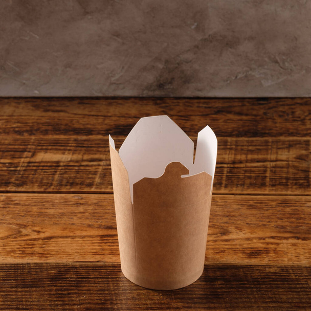 Big brown paper container isolated on wooden background. Eco-friendly disposable food packaging. Preserving nature and recycling concept. - Foto, Imagem