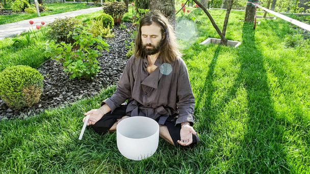 A qigong master conducts meditation using a gong and Crystal bowl, Crystal Tibetian singing bowl, a master meditates receives energy for the body - Photo, Image