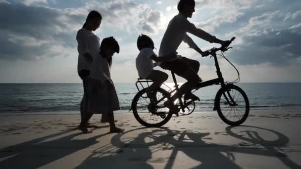 Aasialainen perhe Kesälomalla Neljä ihmistä Isä, äiti, tytär ja poika ajavat polkupyörillä ja kävelevät Illalla auringonlasku rannalla Loma ja matka konsepti. Siluetti hidas liike
 - Materiaali, video