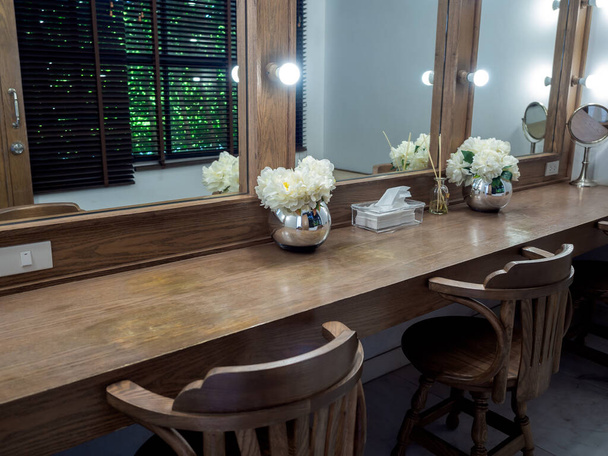Schminkraum klassische und Vintage-Dekoration mit langem Holztisch, Holzstühlen, Spiegel mit Glühbirnen und modernen Blumentopf. - Foto, Bild