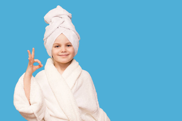 Feliz niña hermosa con toalla en la cabeza mostrar símbolo ok después de aplicar crema quitar el maquillaje disfrutar de un tratamiento de cuidado de la piel hidratado suave limpio sano, aislado en fondo azul
 - Foto, imagen