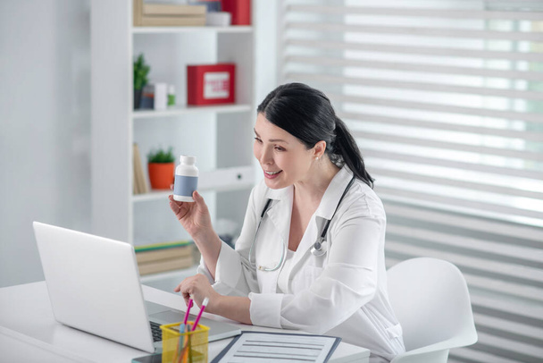 Beautiful woman in white coat with medicine in front of laptop. - 写真・画像