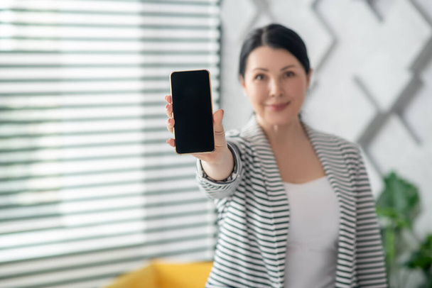 Dark-haired smiling woman showing a smartphone screen. - Foto, Imagen