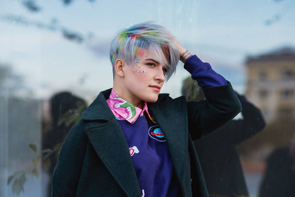 Portrait of a young beautiful woman in green coat with a short haircut and dyed hair. Grey main color and yellow, green, blue and red hair color. - Foto, imagen