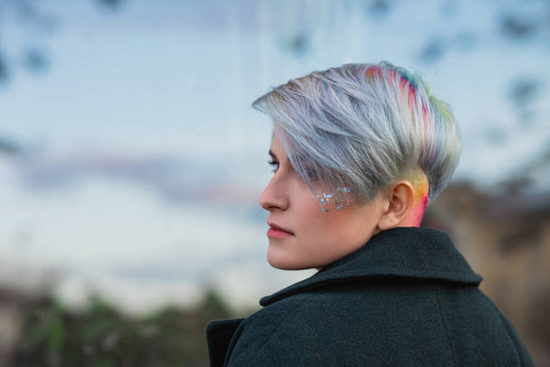 Portrait of a young beautiful woman in green coat with a short haircut and dyed hair. Grey main color and yellow, green, blue and red hair color. - Photo, Image