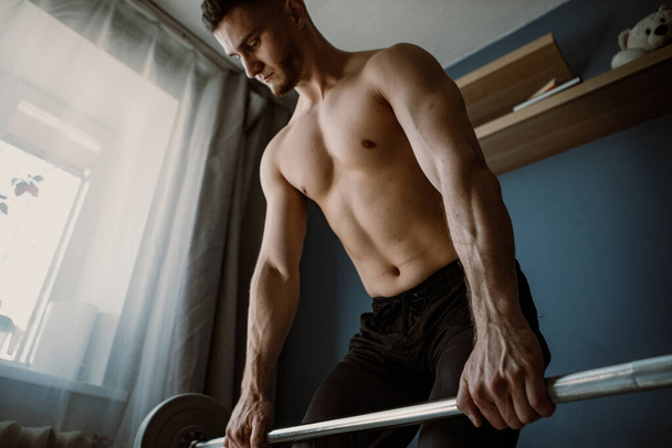handsome guy exercising with barbell in the middle of a room - Фото, изображение