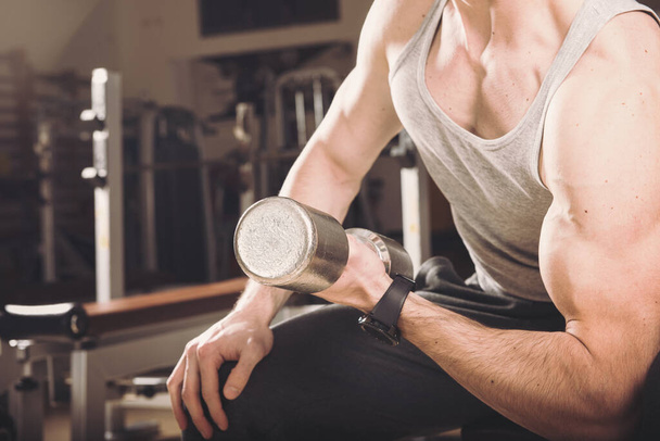Мускулистый человек тренируется в спортзале, делая упражнения с гантелями на бицепсах. Тонкий образ
 - Фото, изображение