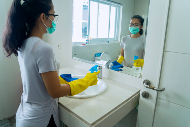 Portrait of young woman cleaning the bathroom using disinfectant while wearing gloves  - Фото, зображення
