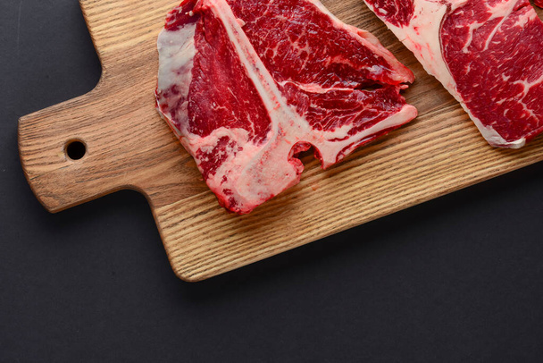 Fresh raw beef steak on wooden cutting board, top view. Served over black background. - Valokuva, kuva