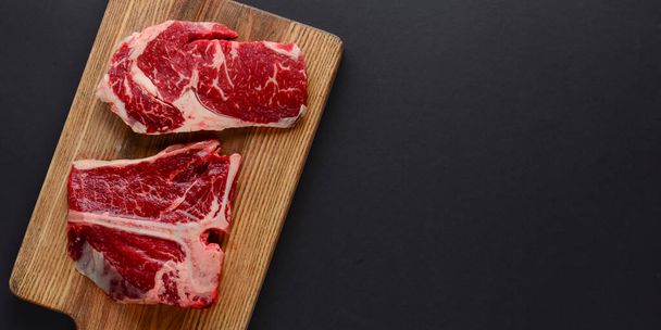 Fresh raw beef steak on wooden cutting board, top view. Served over black background. - Foto, afbeelding