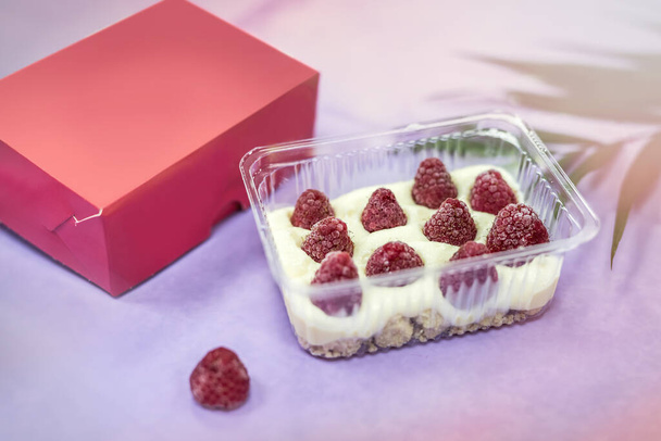 Heerlijk dessert in plastic verpakking met frambozen op tafel en roze wikkeling close-up. Voedselconcept - Foto, afbeelding