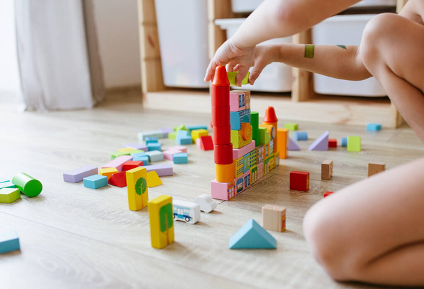 Unrecognizable child playing with colorful wooden building blocks on floor in children room. Selective focus - Foto, imagen