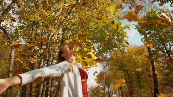 Lány áll a fák alatt kinyújtott karral, ahogy a levelek lehullanak - Felvétel, videó