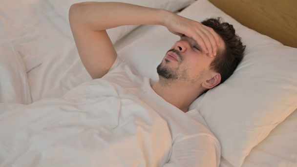 Κουρασμένος νεαρός άνδρας που έχει πονοκέφαλο στο κρεβάτι - Φωτογραφία, εικόνα
