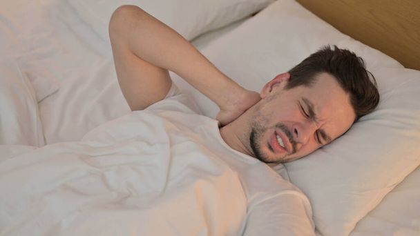 Fáradt fiatalember, akinek nyaki fájdalom az ágyban - Fotó, kép