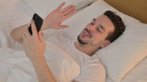 Молодий чоловік робить відео чат на смартфоні в ліжку
 - Фото, зображення