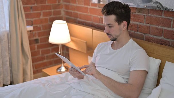 Jeune homme ambitieux utilisant une tablette au lit
 - Photo, image